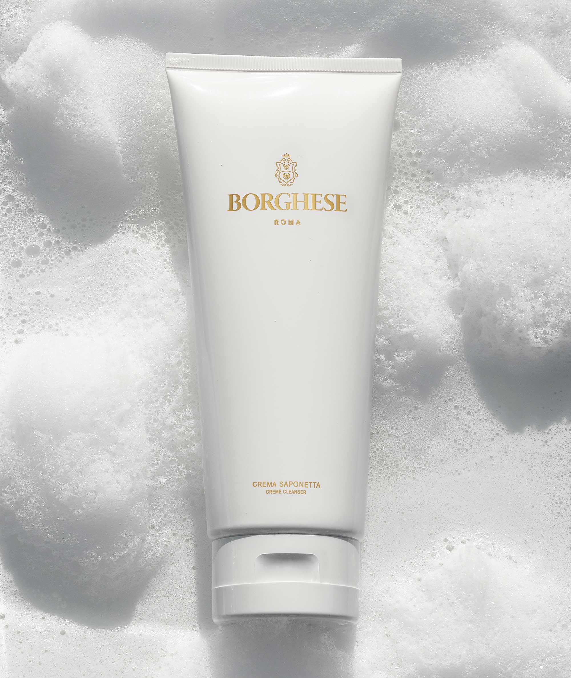 Lifestlye image of Crema Saponetta Cleanser tube on top of a bubbly background, emphasizing its foaming property.